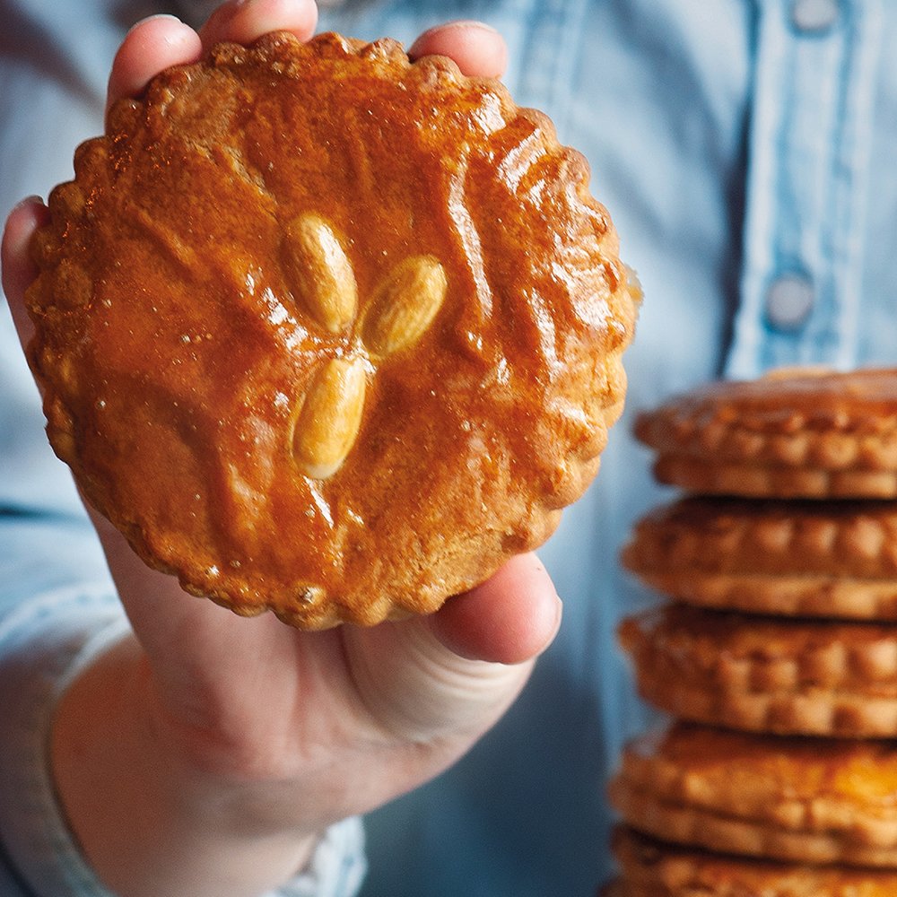 Jan's gevulde koek goudbruin en dubbelgebakken, vastgehouden naast een stapel koeken